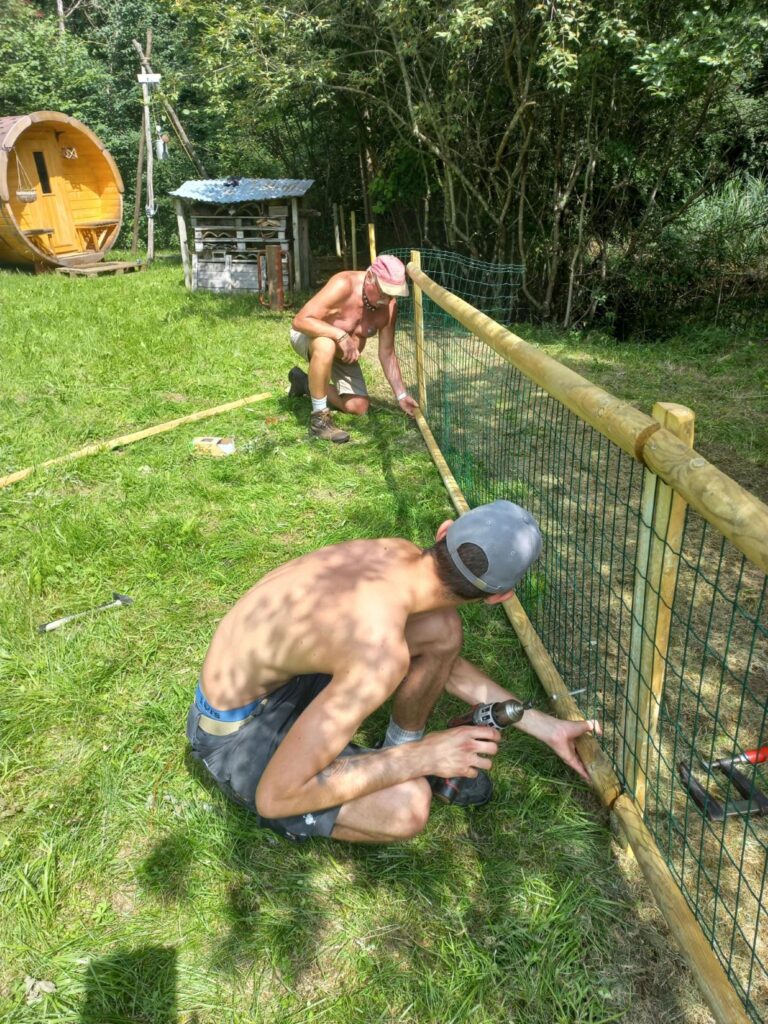 Zwei Männer spannen das Gitter fü einen Weidezaun. es ist heiss.